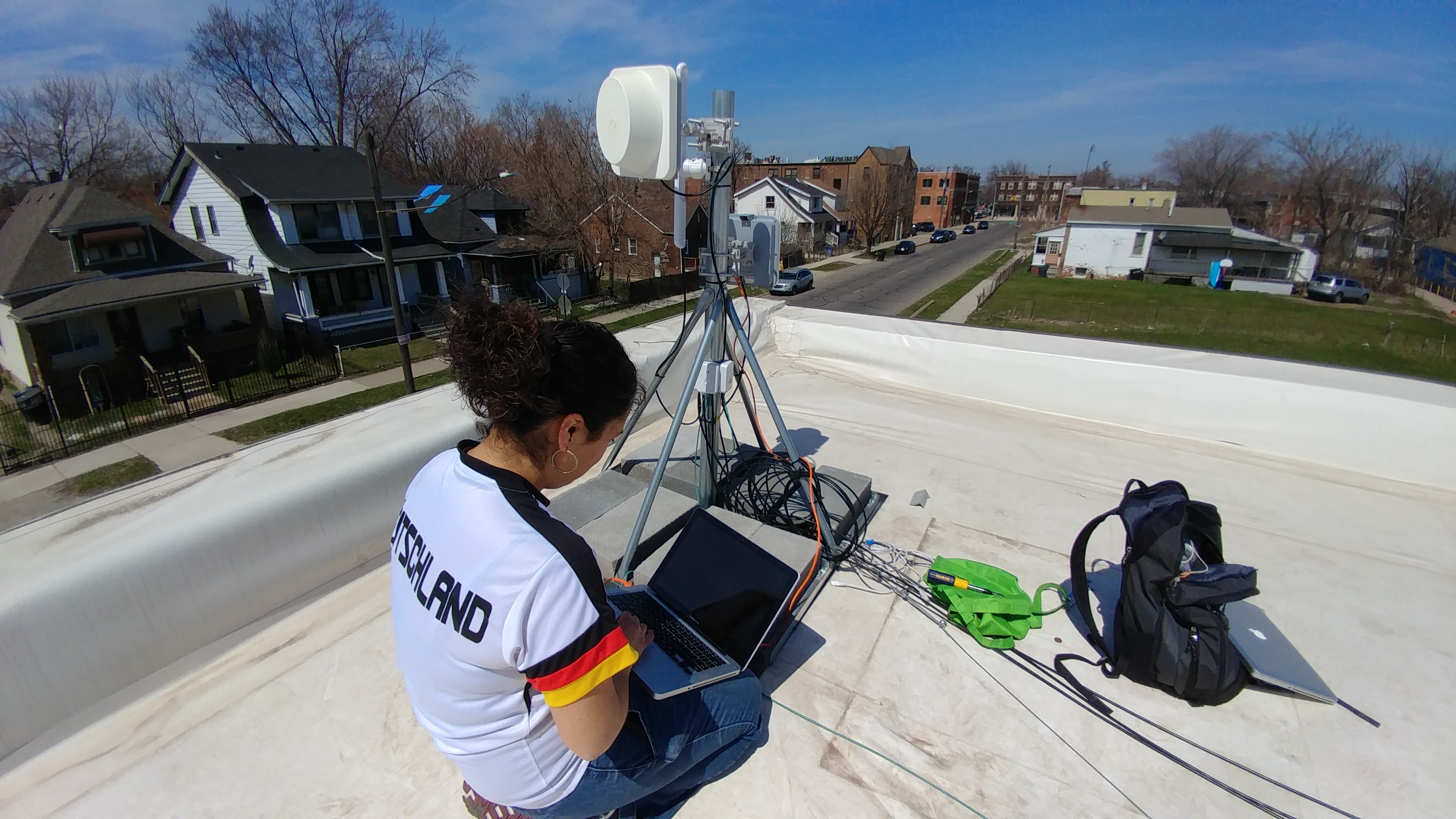 a digital steward on a rooftop, holding a laptop and setting up a large wireless antenna.